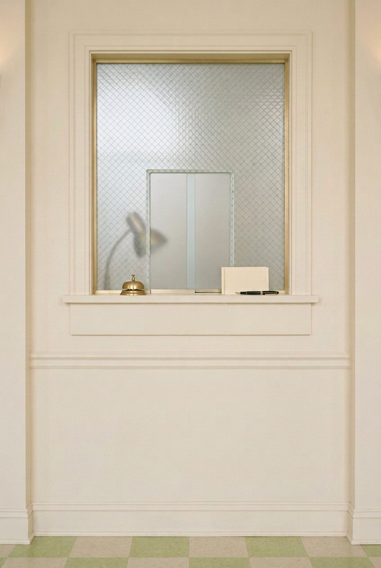 An empty admissions window with frosted glass and a gold service bell